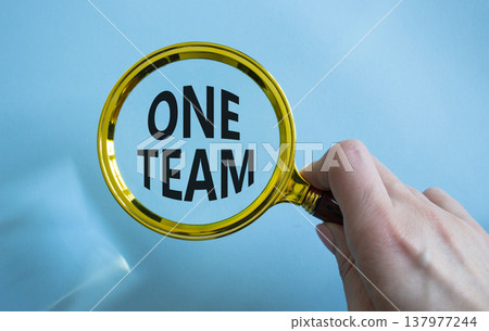 One Team symbol. Magnifying Glass with words One Team. Businessman hand. Beautiful blue background. Business and One Team concept. Copy space. 137977244