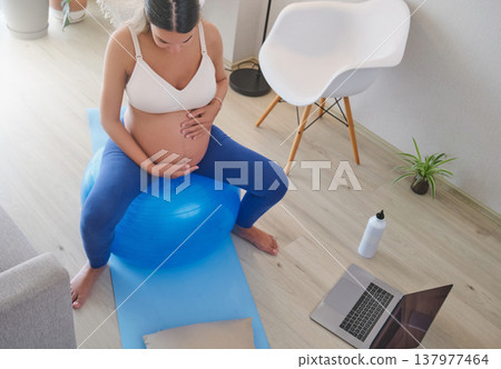Pregnant woman exercising on a fitness ball at home Pregnant woman exercising on a fitness ball at home 137977464