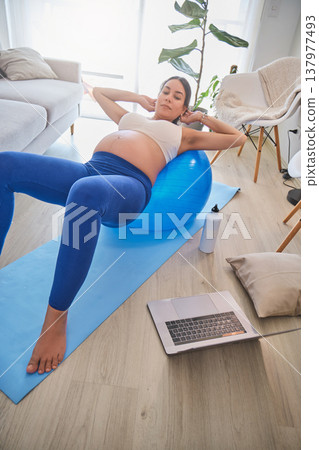 Pregnant woman exercising at home using an exercise ball 137977493