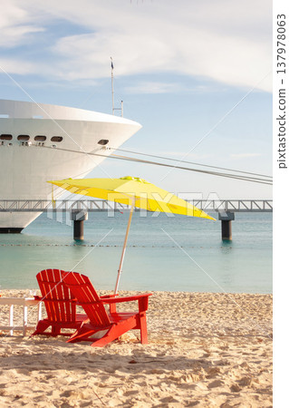 Close-up of beach chair and colourful napkins on the sand of a Bahamian beach. A cruise ship at anchor in the background Tourism and holiday concept Close-up of beach chair and colourful napkins on the sand of a Bahamian beach. A cruise ship at anchor in the background Tourism and holiday concept 137978063
