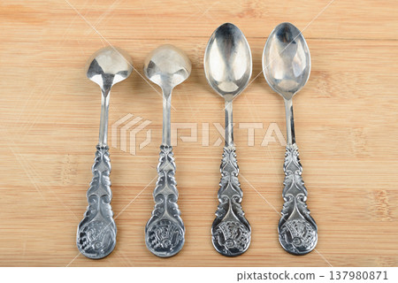 Four elegant vintage teaspoons arranged in a row on a wooden stand. 137980871