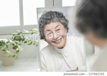 An 80-year-old woman smiles while looking in a mirror. Skincare & Beauty Image An 80-year-old woman smiles while looking in a mirror. Skincare & Beauty Image 137981505