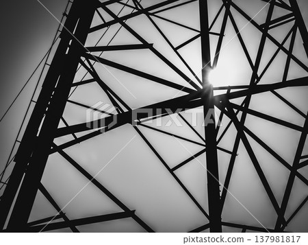 A monochrome industrial image of a transmission tower silhouette against a dark, cloudy sky. A monochrome industrial image of a transmission tower silhouette against a dark, cloudy sky. 137981817