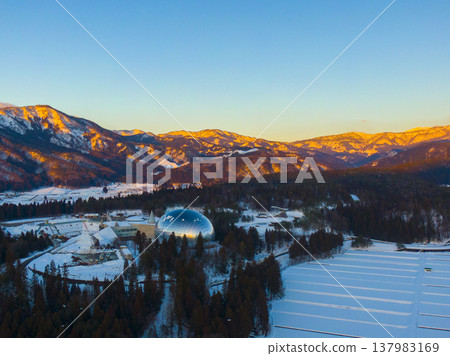 Snow-covered mountains bathed in the setting sun and the Fukui Prefectural Dinosaur Museum: Winter aerial photography by drone Snow-covered mountains bathed in the setting sun and the Fukui Prefectural Dinosaur Museum: Winter aerial photography by drone 137983169