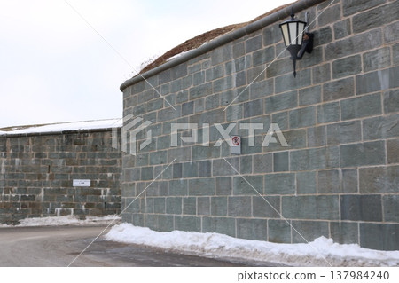 A scene of stone walls with lingering snow and a curved street. 137984240