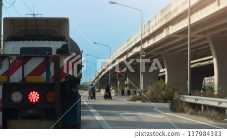Rear side of truck car with turn on brake light. Stop by traffic red light control with two motorcycles parked right in front of the intersection. Concrete overpass bridge on the side of the road. 137984383