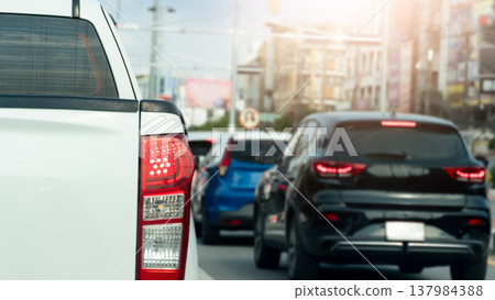Rear side of pikup white car with turn on brake light. Traffic jam on the asphalt road with many car in the city. Background blurred of town in Rayong Thailand. 137984388