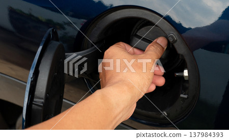 Close up shot of a black plastic fuel gas cap with a ridged edge for easy gripping. Handle to twist the fuel filler cap open or close. A luxurious dark blue car. Close up shot of a black plastic fuel gas cap with a ridged edge for easy gripping. Handle to twist the fuel filler cap open or close. A luxurious dark blue car. 137984393