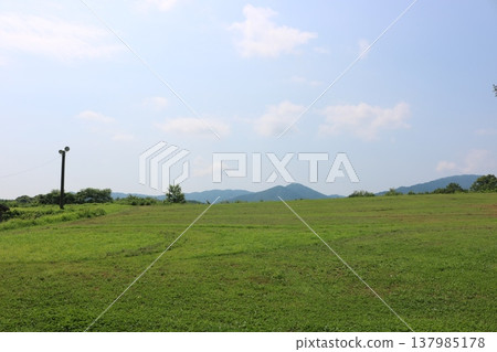 A simple natural landscape of blue sky and grasslands, with distant mountain ranges. 137985178
