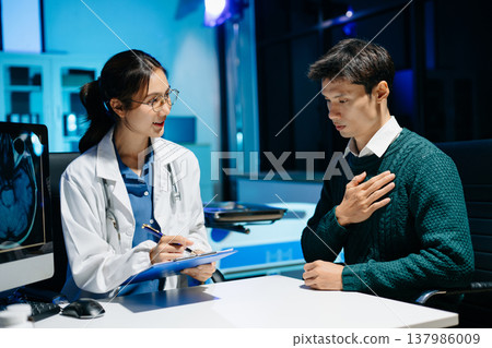 Female doctor reviewing brain MRI and notes during medical consultation with stressed male patient. Neurology diagnosis, mental health care and modern healthcare technology. Female doctor reviewing brain MRI and notes during medical consultation with stressed male patient. Neurology diagnosis, mental health care and modern healthcare technology. 137986009