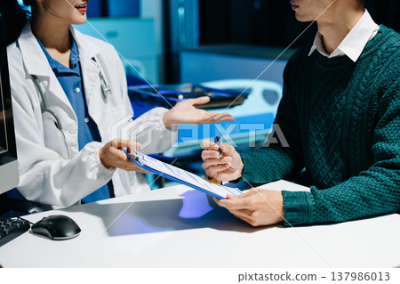 Doctor explains medical form as patient signs consent in modern clinic. Healthcare, insurance, medical consultation, diagnosis, treatment, documentation concept. Doctor explains medical form as patient signs consent in modern clinic. Healthcare, insurance, medical consultation, diagnosis, treatment, documentation concept. 137986013