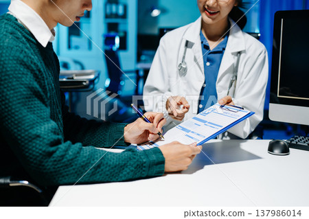 Doctor explains medical form as patient signs consent in modern clinic. Healthcare, insurance, medical consultation, diagnosis, treatment, documentation concept. Doctor explains medical form as patient signs consent in modern clinic. Healthcare, insurance, medical consultation, diagnosis, treatment, documentation concept. 137986014