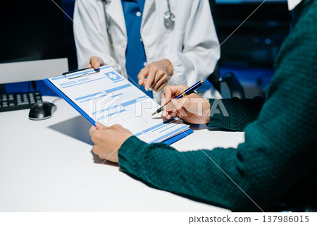 Doctor explains medical form as patient signs consent in modern clinic. Healthcare, insurance, medical consultation, diagnosis, treatment, documentation concept. 137986015