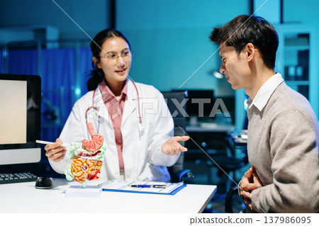 Doctor explains digestive system using anatomy model during consultation with patient suffering abdominal pain. Gastroenterology, diagnosis, treatment, healthcare concept. 137986095