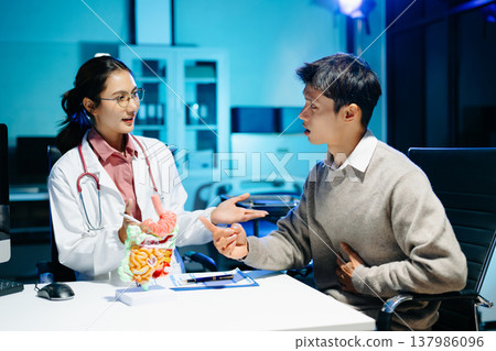 Doctor explains digestive system using anatomy model during consultation with patient suffering abdominal pain. Gastroenterology, diagnosis, treatment, healthcare concept. 137986096