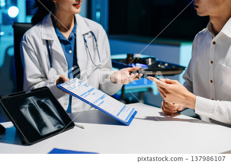 Asian doctor consulting patient in modern hospital office, explaining medical report and providing professional healthcare advice with trust 137986107