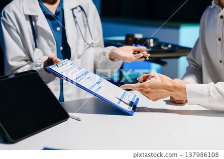 Asian doctor consulting patient in modern hospital office, explaining medical results and giving professional healthcare advice with friendly communication. 137986108