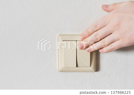 Hand turning off light switch on white wall, saving electricity Hand turning off light switch on white wall, saving electricity 137986225