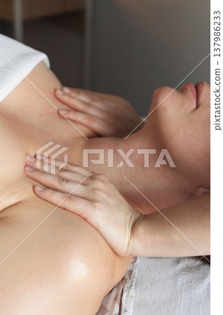 Woman lying on a massage table receiving a professional back and shoulder massage in a relaxing spa environment with candles Woman lying on a massage table receiving a professional back and shoulder massage in a relaxing spa environment with candles 137986233