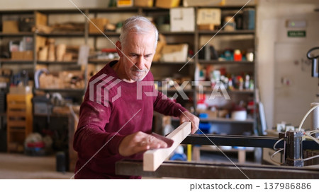 Mature carpenter sanding wood plank in workshop 137986886