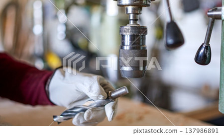 Person changing drill bit on a machine press in workshop 137986891