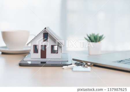 Home buying and mortgage planning concept for real estate investment and insurance, featuring a miniature house, keys, calculator, pen and contract on a bright desk in a modern office. real estate 137987625