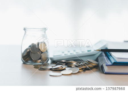 Coin jar and stacked coins beside calculator on financial documents, symbolizing savings, budgeting, accounting and investment planning for personal finance and business growth strategy. investment 137987668