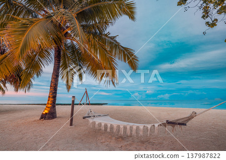 Tranquil sunset with hammock between palm trees, golden sky reflecting on calm tropical ocean, serene summer vacation tropical paradise background 137987822