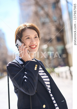 一位三十多歲的日本女商人一邊走在街上，一邊用智慧型手機通話。 137987985