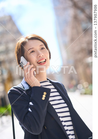 一位三十多歲的日本女商人一邊走在街上,一邊用智慧型手機通話。 一位三十多歲的日本女商人一邊走在街上,一邊用智慧型手機通話。 137987986