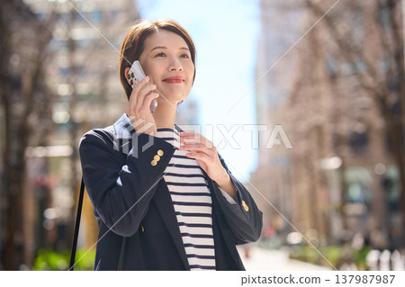 一位三十多歲的日本女商人一邊走在街上，一邊用智慧型手機通話。 137987987