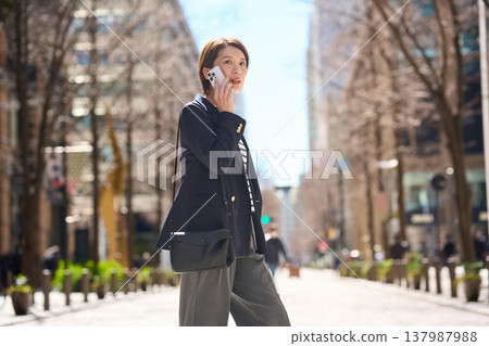 一位三十多歲的日本女商人一邊走在街上,一邊用智慧型手機通話。 一位三十多歲的日本女商人一邊走在街上,一邊用智慧型手機通話。 137987988