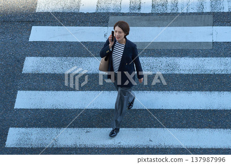 A Japanese businesswoman in her 30s talks on her smartphone while walking down the street. A Japanese businesswoman in her 30s talks on her smartphone while walking down the street. 137987996