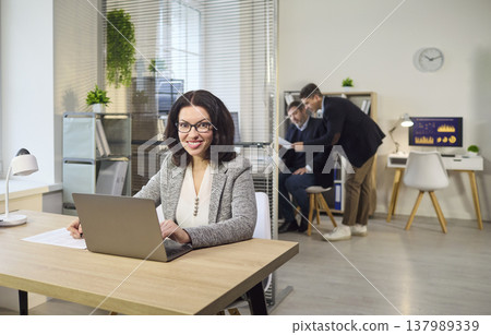 Confident businesswoman doing financial analysis on laptop in modern office Confident businesswoman doing financial analysis on laptop in modern office 137989339