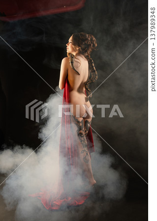 Artistic portrait of a tattooed woman's back with a python and red fabric in fog Artistic portrait of a tattooed woman's back with a python and red fabric in fog 137989348