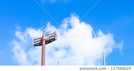 A simple scene with a refreshing blue sky, white clouds, and stadium lights. A simple scene with a refreshing blue sky, white clouds, and stadium lights. 137989820