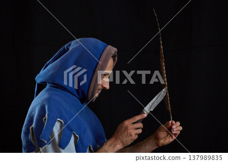 A profile portrait of a man in a medieval hood holding a knife and feather A profile portrait of a man in a medieval hood holding a knife and feather 137989835