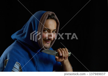 Portrait of a smiling man in a medieval hood holding a knife Portrait of a smiling man in a medieval hood holding a knife 137989837