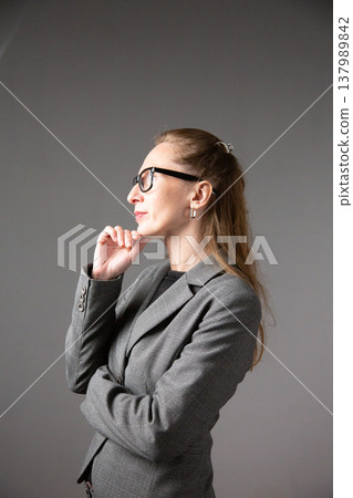 A profile portrait of a woman with glasses and long hair in a business suit, lost in thought and touching her chin A profile portrait of a woman with glasses and long hair in a business suit, lost in thought and touching her chin 137989842