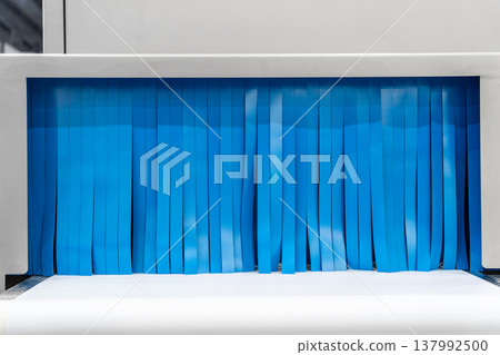 Close-up view of empty white narrow conveyer belt and blue curtain of x-ray inspecting machine in industrial building. Soft focus. Copy space. Manufacturing and production line theme. Close-up view of empty white narrow conveyer belt and blue curtain of x-ray inspecting machine in industrial building. Soft focus. Copy space. Manufacturing and production line theme. 137992500