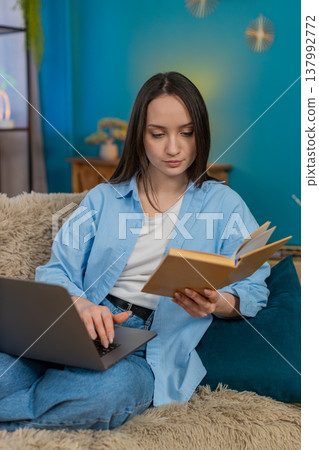 Young woman studying online with laptop and book making notes seriously focused distance education Young woman studying online with laptop and book making notes seriously focused distance education 137992772