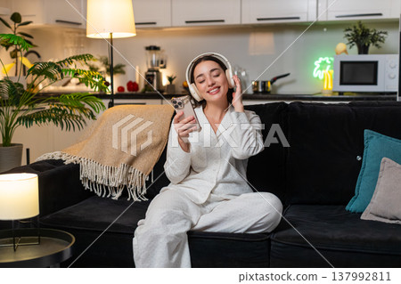 Young woman relaxes with wireless headphones plays music eyes closed smile calm head nod evening zen Young woman relaxes with wireless headphones plays music eyes closed smile calm head nod evening zen 137992811