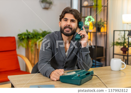 Indian man talks on retro wired telephone from nineties smiles places handset back on base with care Indian man talks on retro wired telephone from nineties smiles places handset back on base with care 137992812