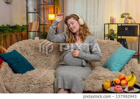 Pregnant young woman dancing with headphones, gently touching belly smiling positive mood and energy Pregnant young woman dancing with headphones, gently touching belly smiling positive mood and energy 137992943