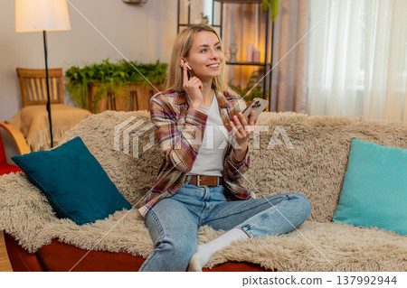 Adult woman listening to voice message with wireless earphones at home surprised by unexpected audio Adult woman listening to voice message with wireless earphones at home surprised by unexpected audio 137992944