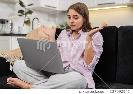 Young woman sees failed task on laptop spreads hands unsure breathes deep plans new approach to work Young woman sees failed task on laptop spreads hands unsure breathes deep plans new approach to work 137992945