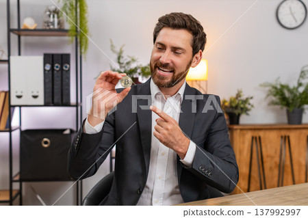 Middle-aged businessman shows Bitcoin golden coin spins it recommending crypto investment to viewers Middle-aged businessman shows Bitcoin golden coin spins it recommending crypto investment to viewers 137992997