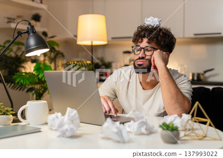 Arabian man frustrated with creative block sits with crumpled papers on desk writes ideas at night 137993022