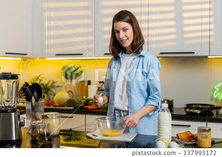 Young woman happily whisking eggs in bowl in home kitchen for healthy diet meal prep easy breakfast 137993172