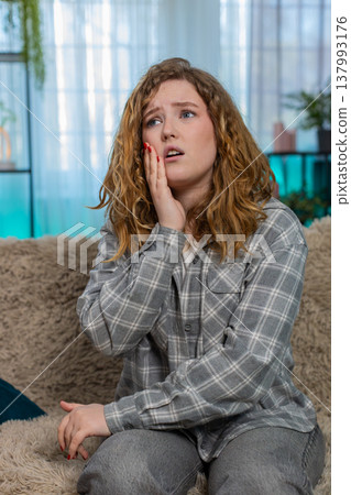 Woman sitting on sofa holding cheek with hand suffering from sharp toothache feeling pain and stress Woman sitting on sofa holding cheek with hand suffering from sharp toothache feeling pain and stress 137993176